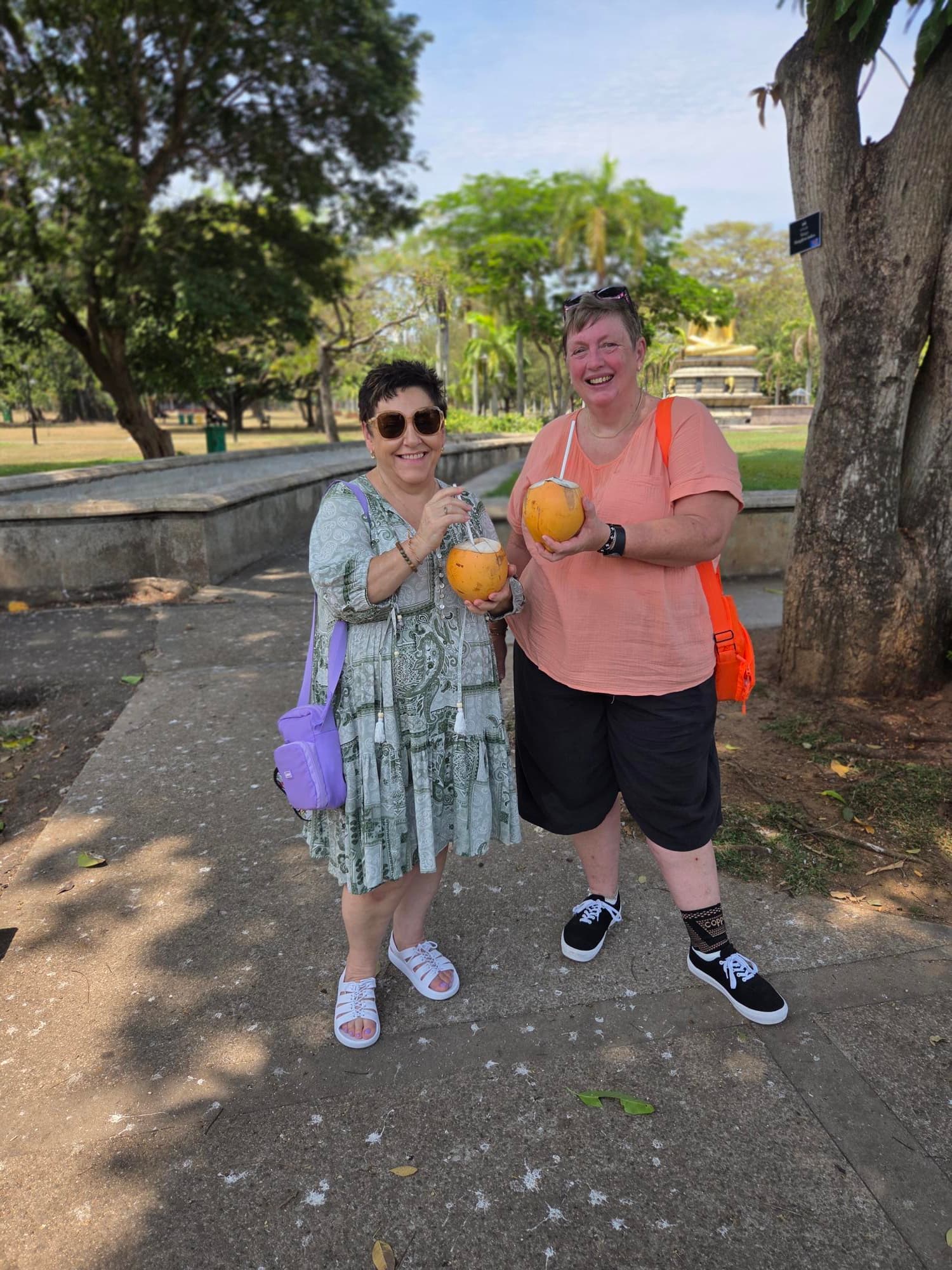 Kay and Karen smiling together while holding coconuts on holiday